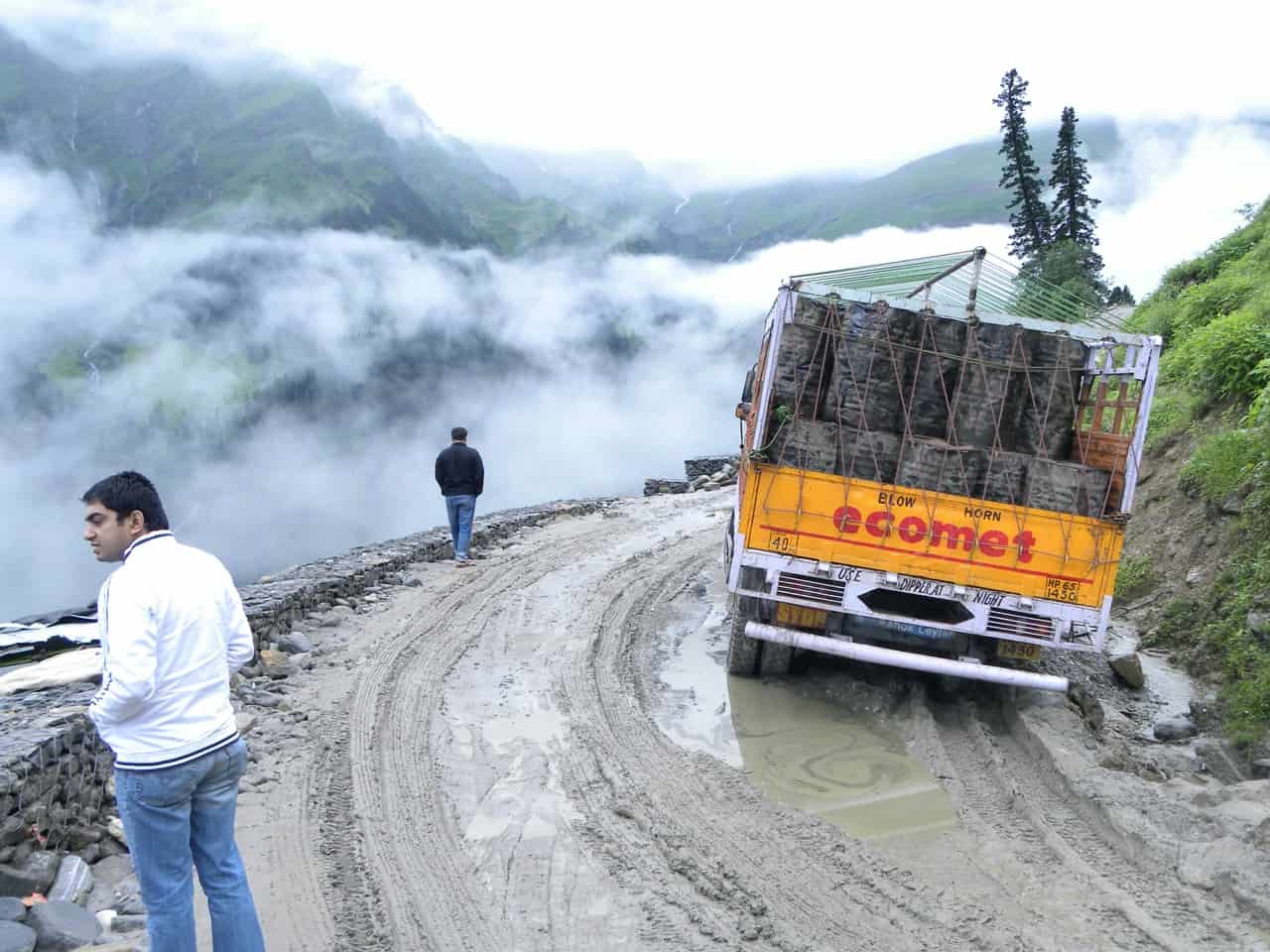 Slushy monsoon road from Manali toward Rohtang with a truck stuck in mud and clouds filling the valley