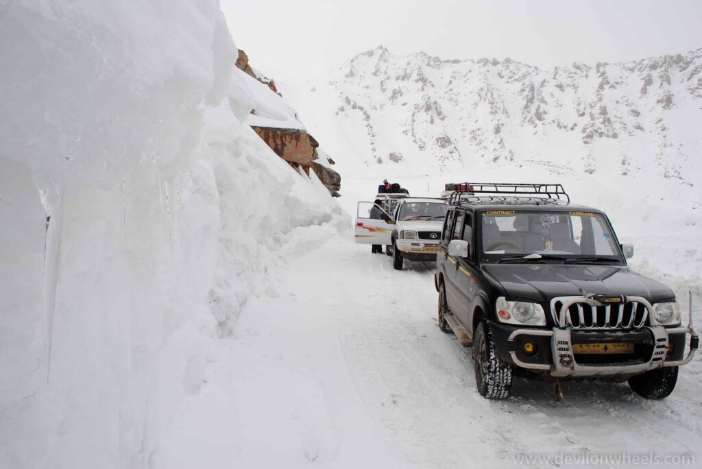 SUVs driving between high snow walls on a mountain pass road in Ladakh
