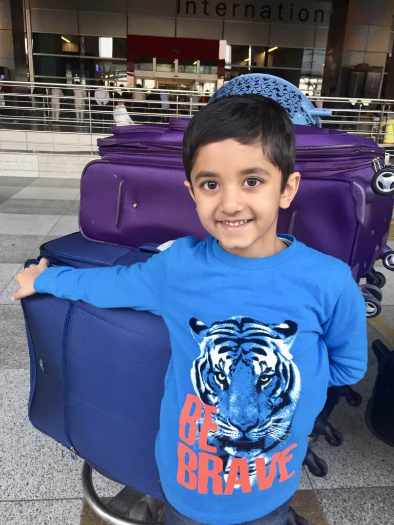 Young boy standing beside suitcases on a luggage trolley outside an international airport terminal