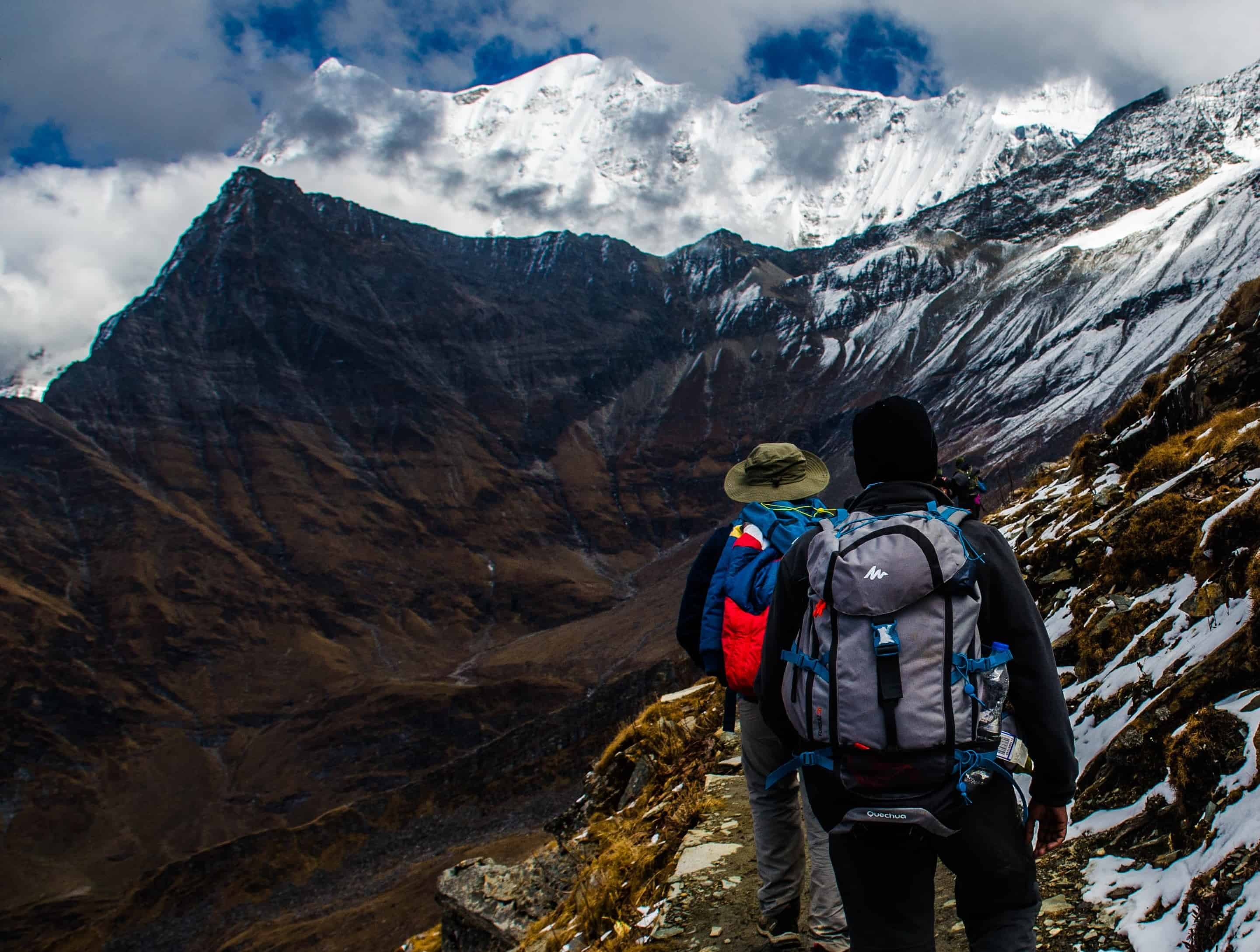 Two backpackers with loaded rucksacks walking a snowy Himalayan trail