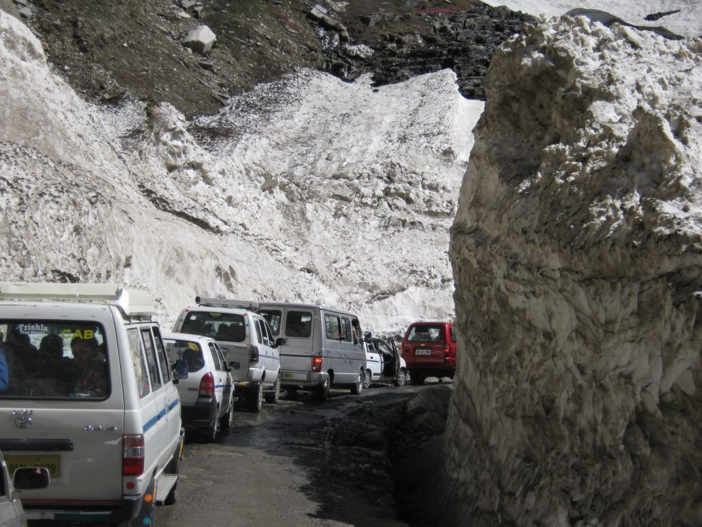 Vehicles between cleared snow walls on a high-altitude Himalayan road in early season