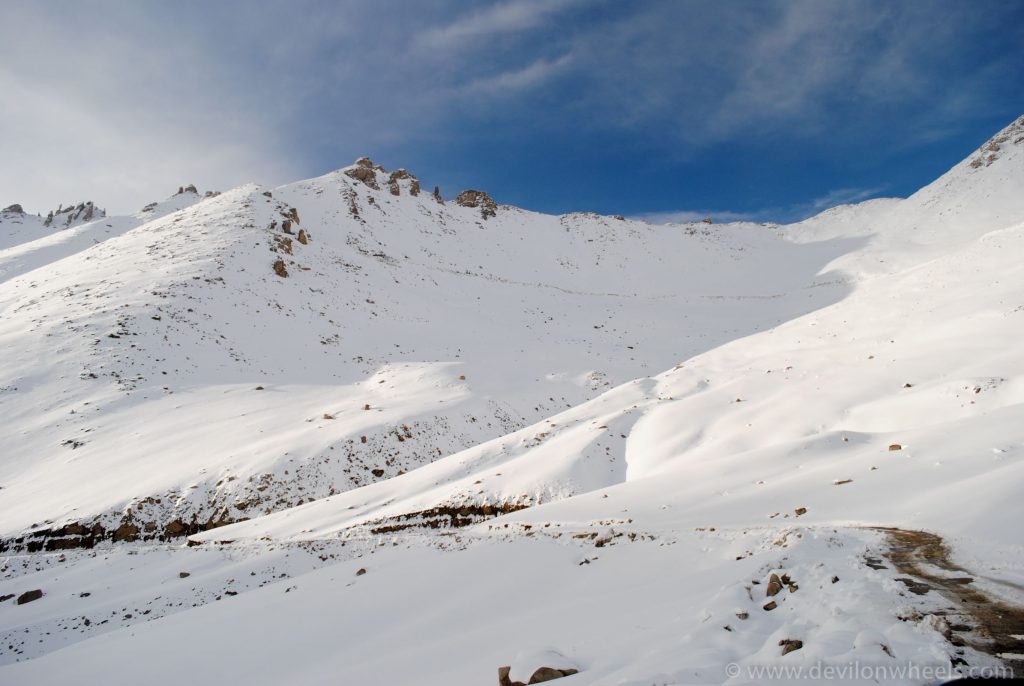 Snow-covered slopes at Khardung La pass in Ladakh under a blue sky
