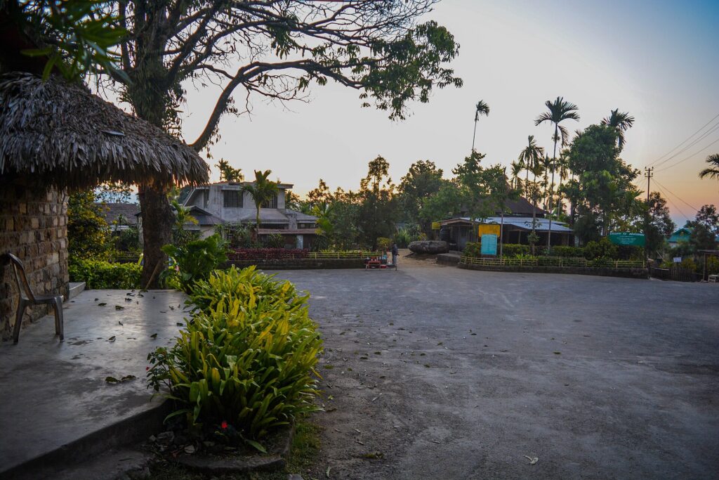 Mawlynnong village square at dusk with thatched hut and areca palms in Meghalaya